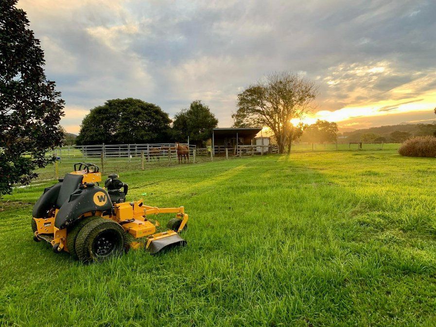 A Yellow Lawn Mower Is Parked in A Grassy Field — All Round Ground Maintenance in Woolgoolga, NSW