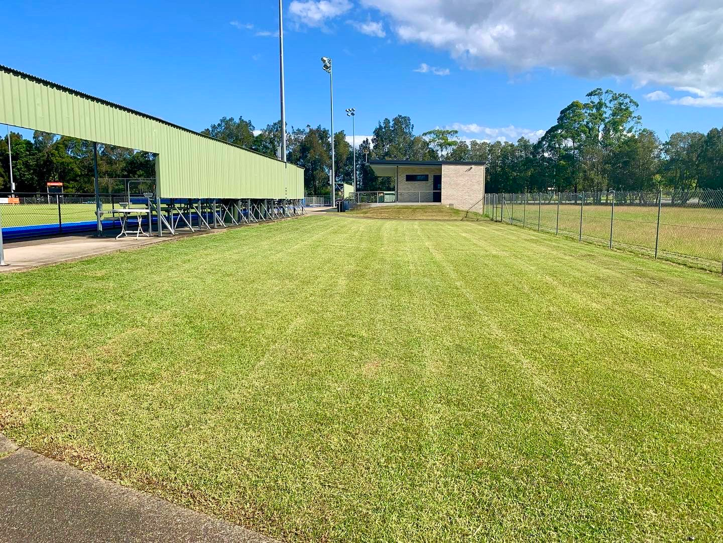A Lush Green Field with A Fence and A Building — All Round Ground Maintenance in Woolgoolga, NSW