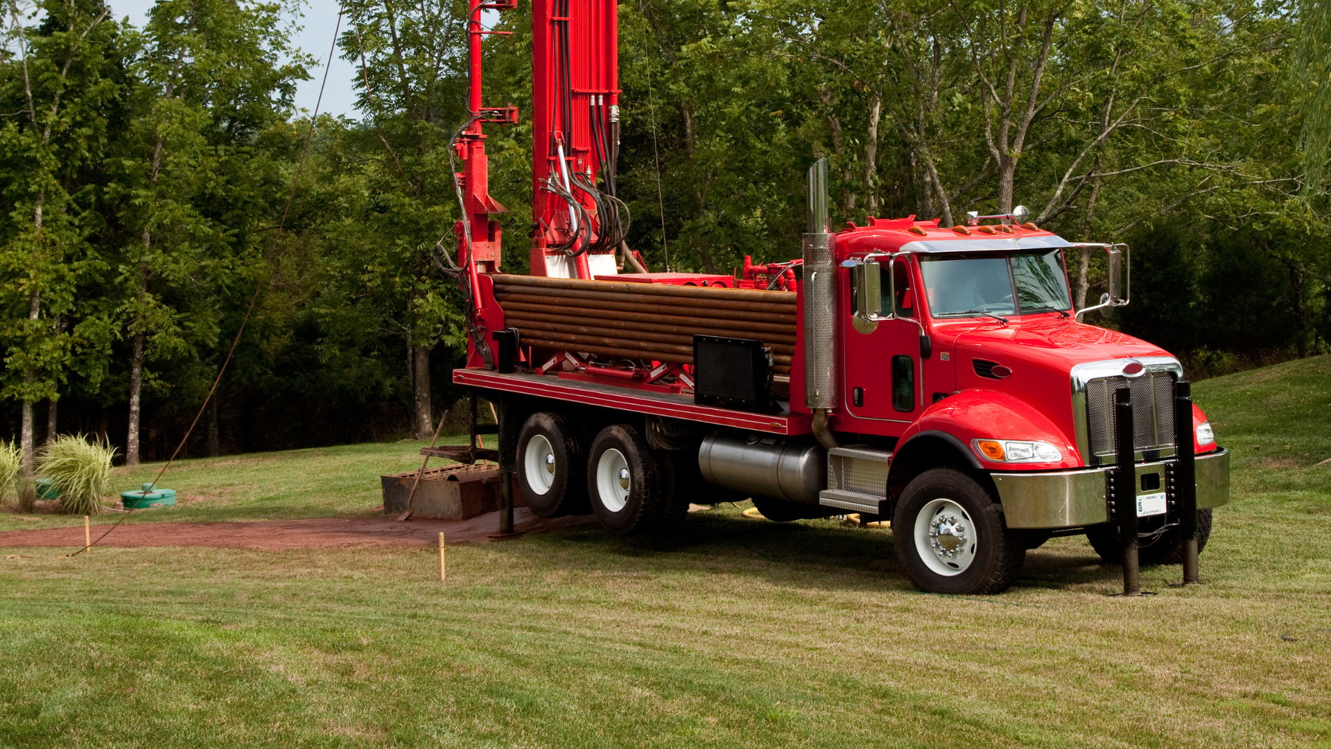 A red truck is parked in a grassy field with trees in the background.