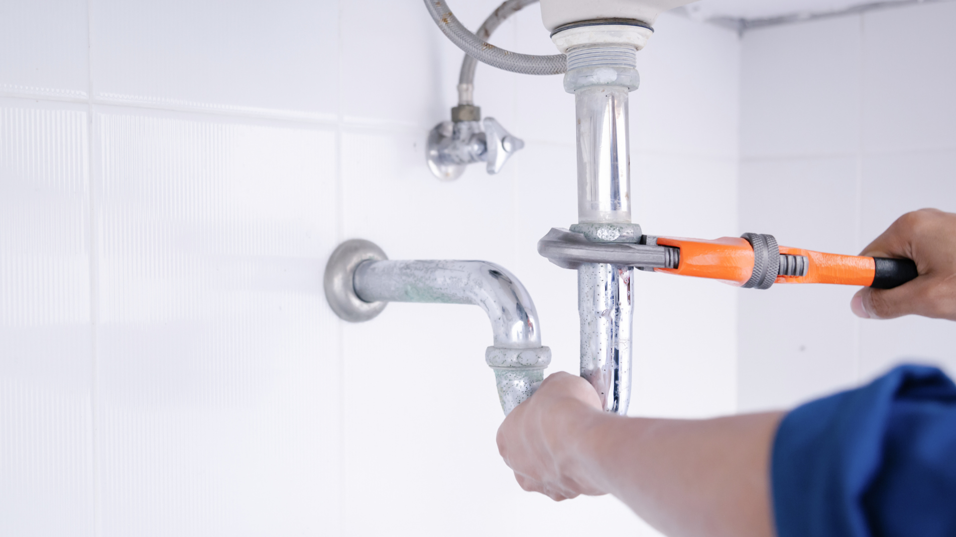 A plumber is fixing a sink pipe with a wrench.