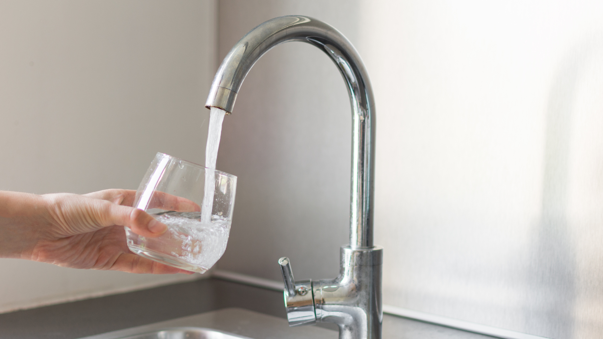 A person is pouring water into a glass from a faucet.