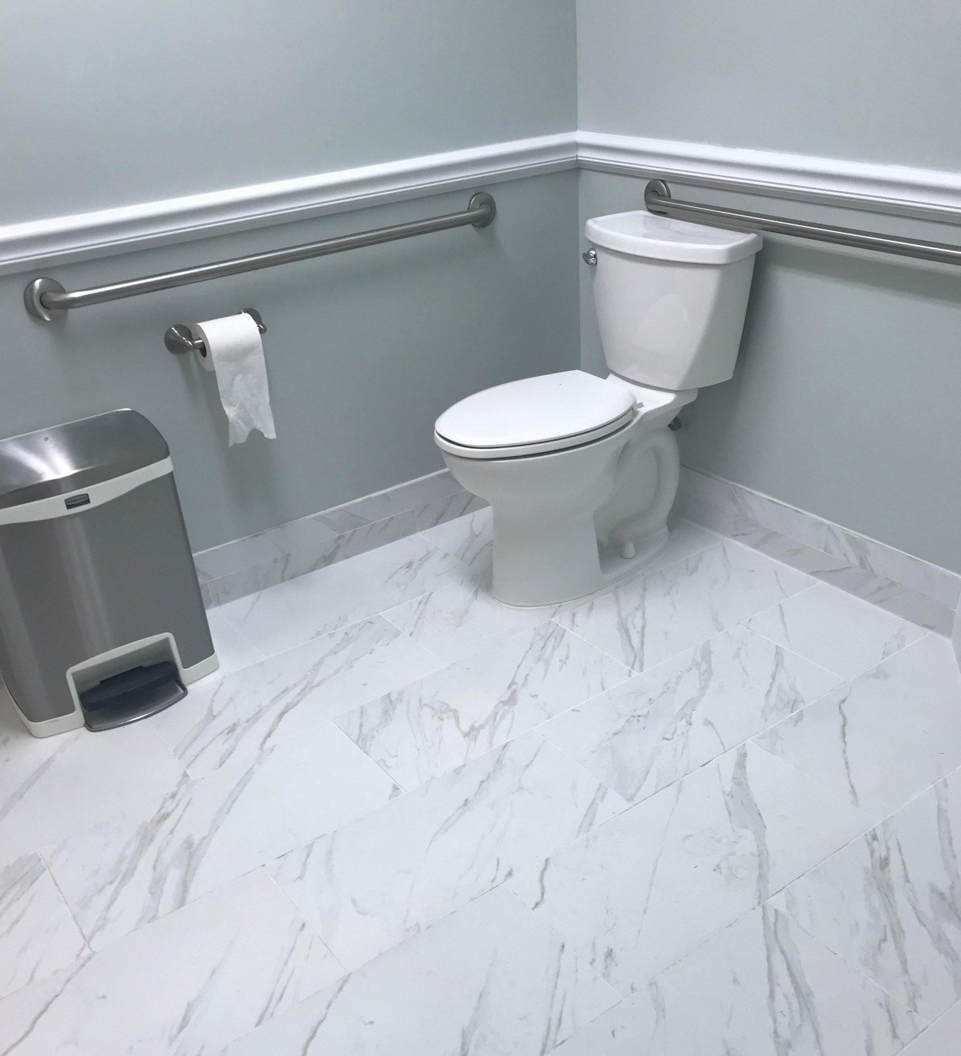 A bathroom with a toilet , trash can , and handrails
