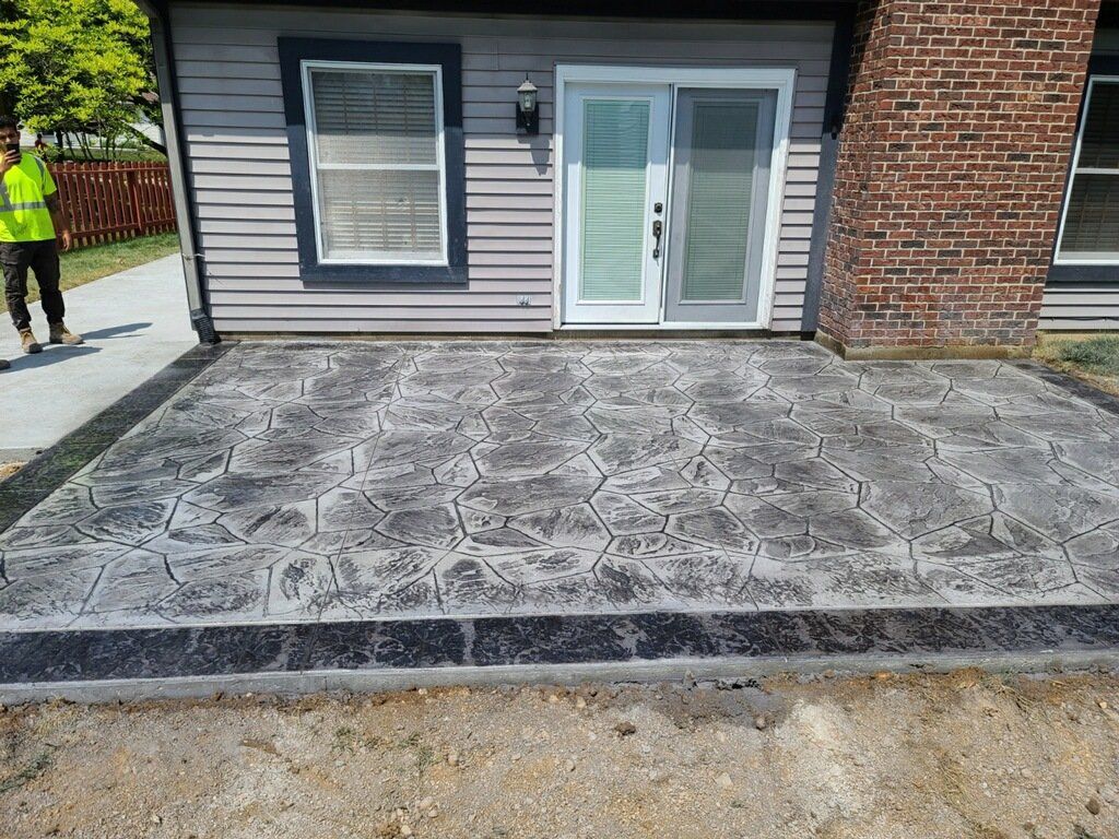 A man is standing in front of a brick house with a patio in front of it.