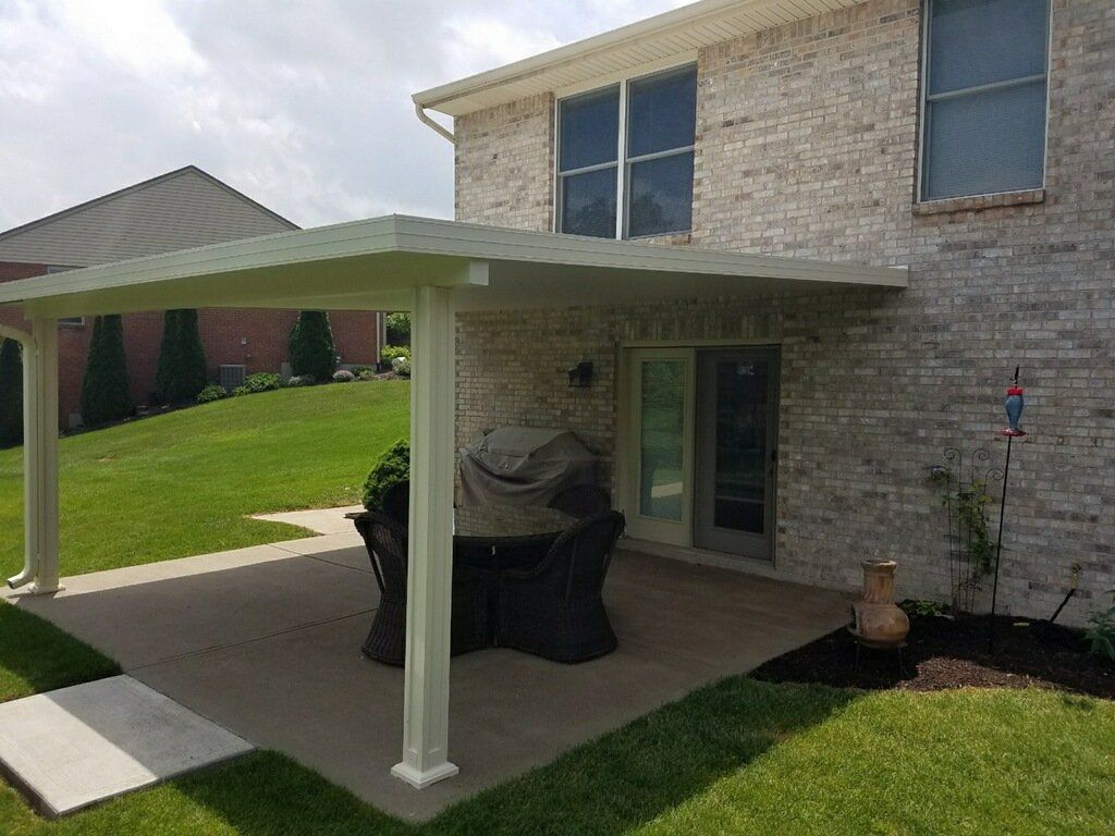 There is a patio with a table and chairs under a covered patio cover.