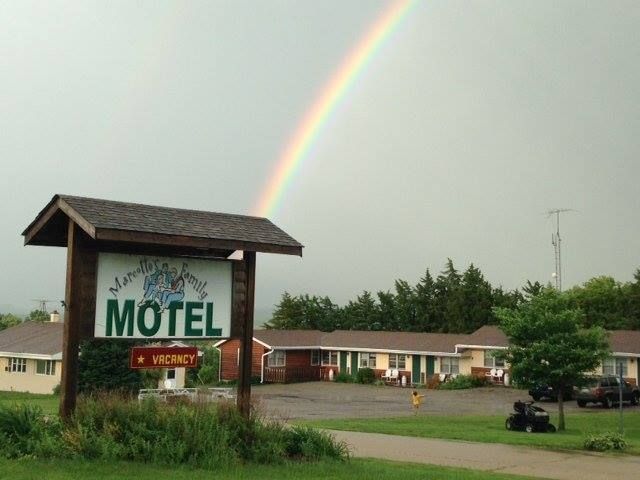 Rainbow arching over the sign of a motel, which is shown in front of a row of buildings.