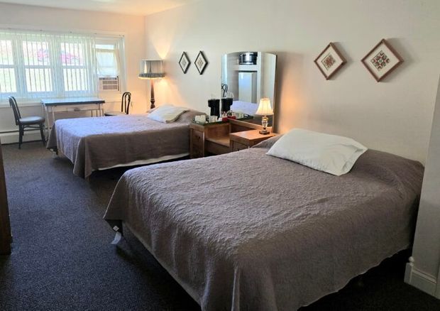 Two beds in a hotel room. Beige bedding, dark carpet, and a window.