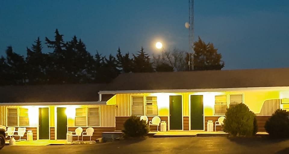 A motel at night; illuminated rooms, bright moon in the background, trees, and radio tower.
