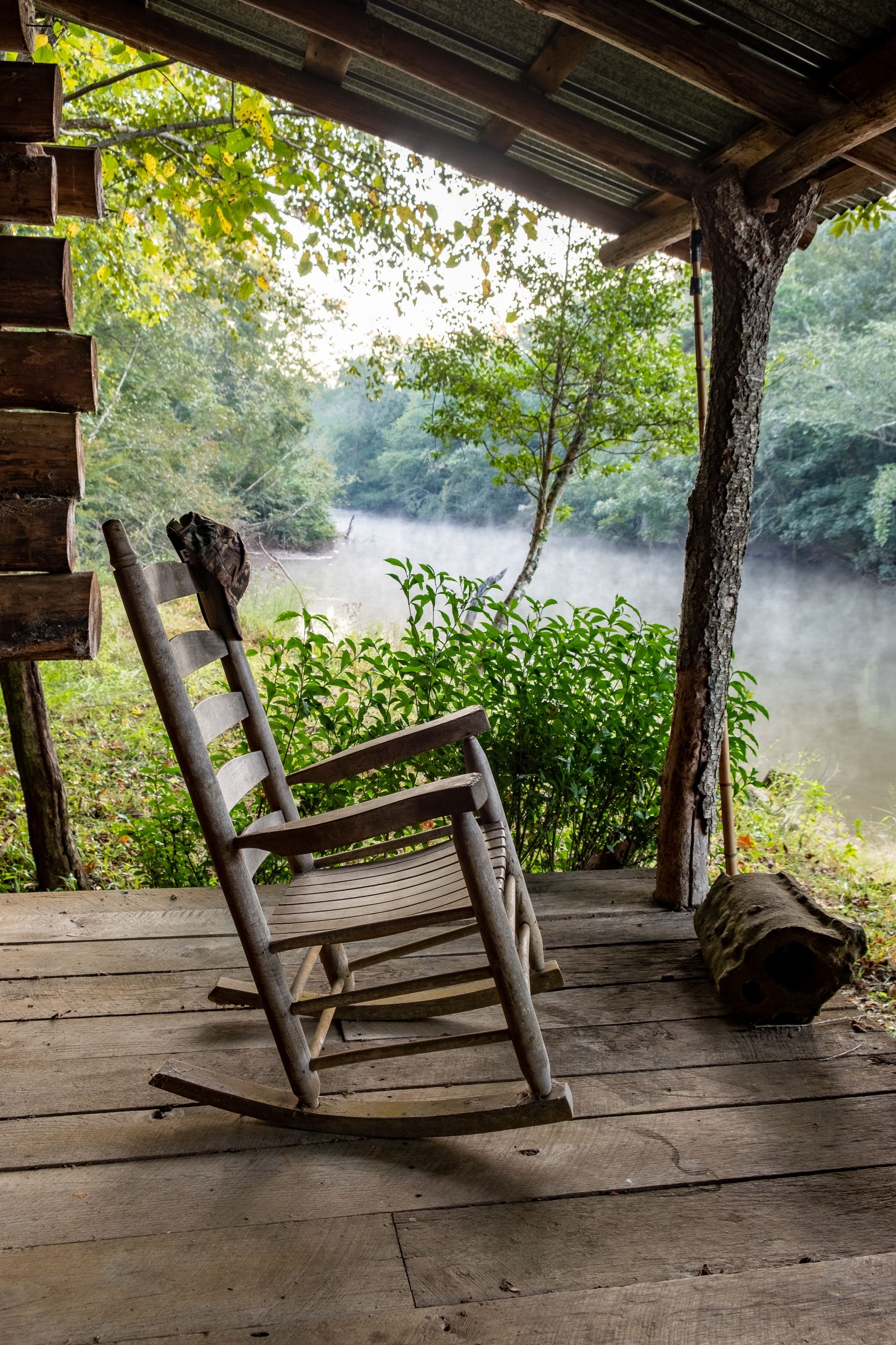 Wooden rocking chair on a porch overlooking a foggy river.