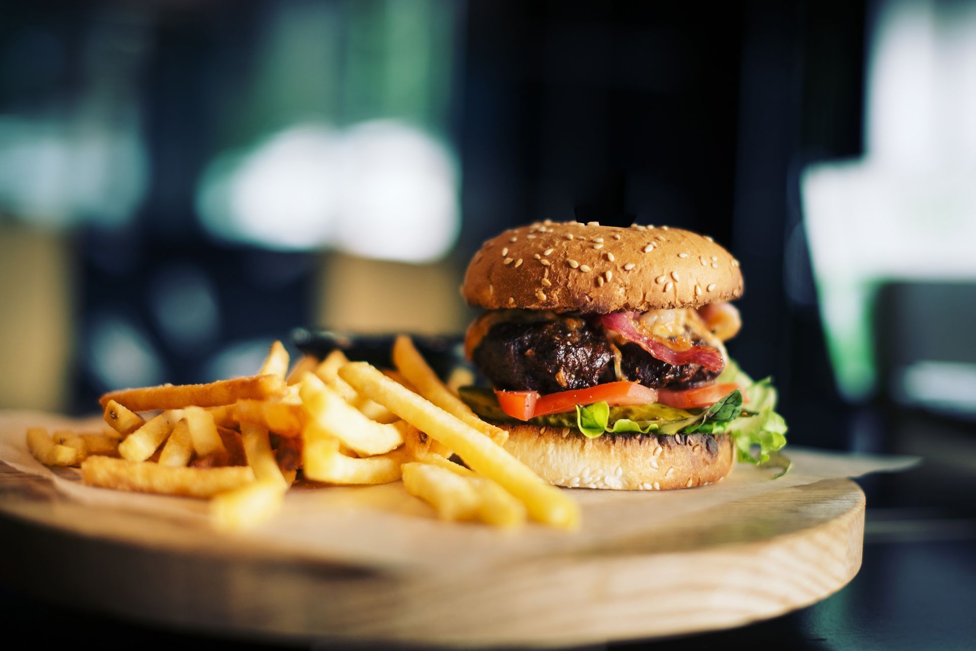 Hamburger with fries on a wooden board, with blurred background.