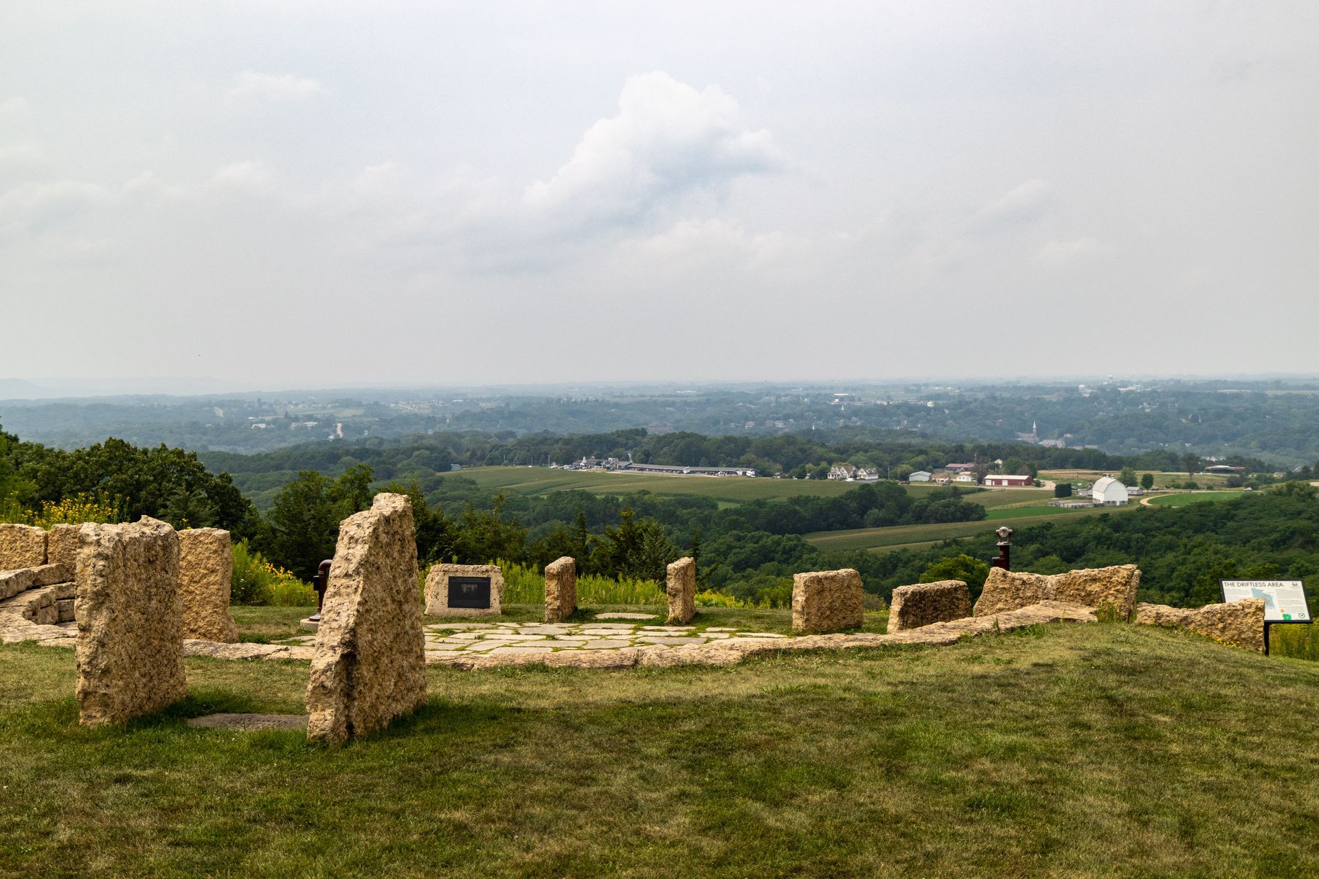 Stone ruins on a hilltop overlooking a valley with trees and buildings under a cloudy sky.