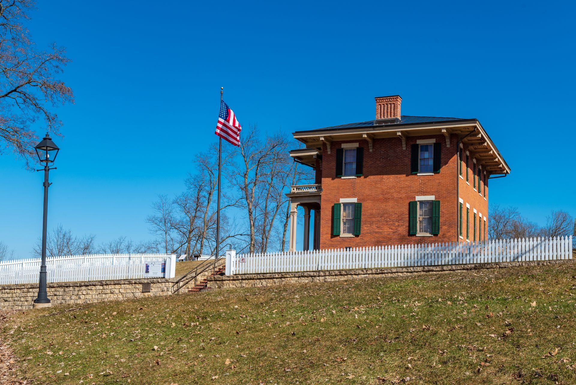 Red brick house with an American flag, white fence, and a blue sky.
