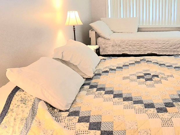 Bedroom with two beds, one with white pillows, a lamp, and a window with blinds.