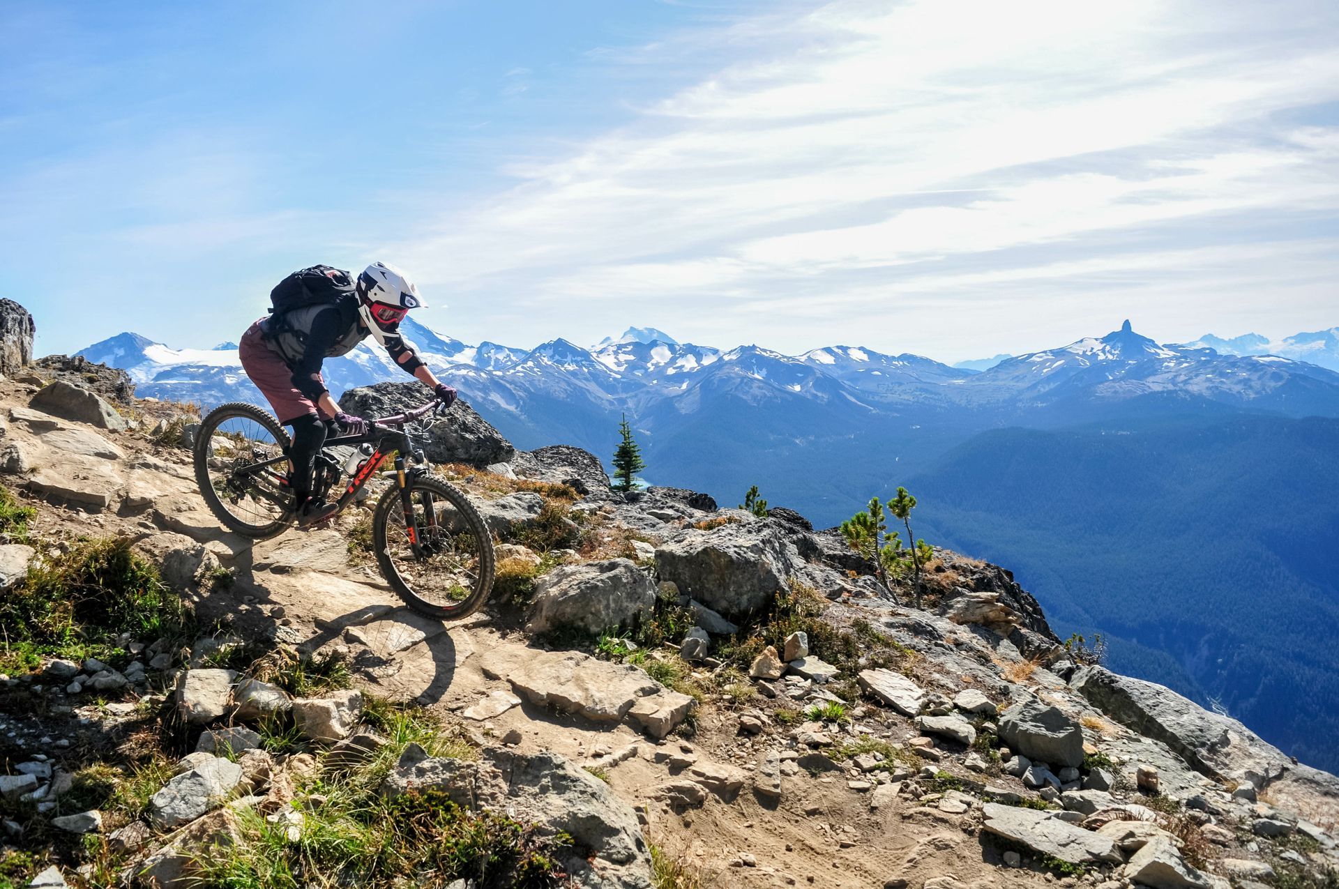 Mountain biker descending a rocky alpine trail with snow-capped peaks in the background