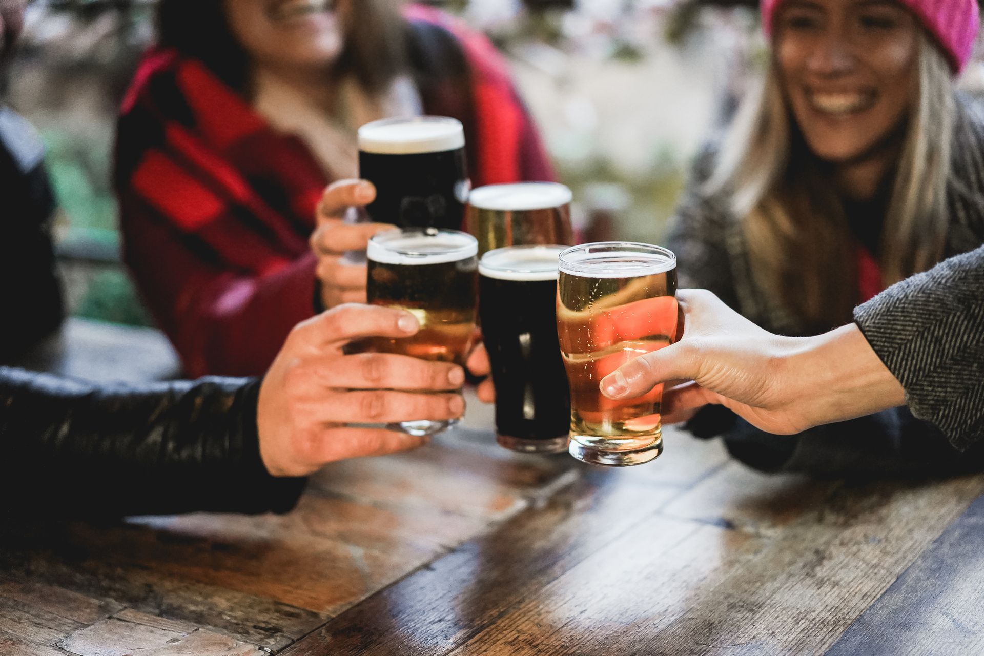 Friends clinking beer glasses over a wooden table in a lively outdoor setting