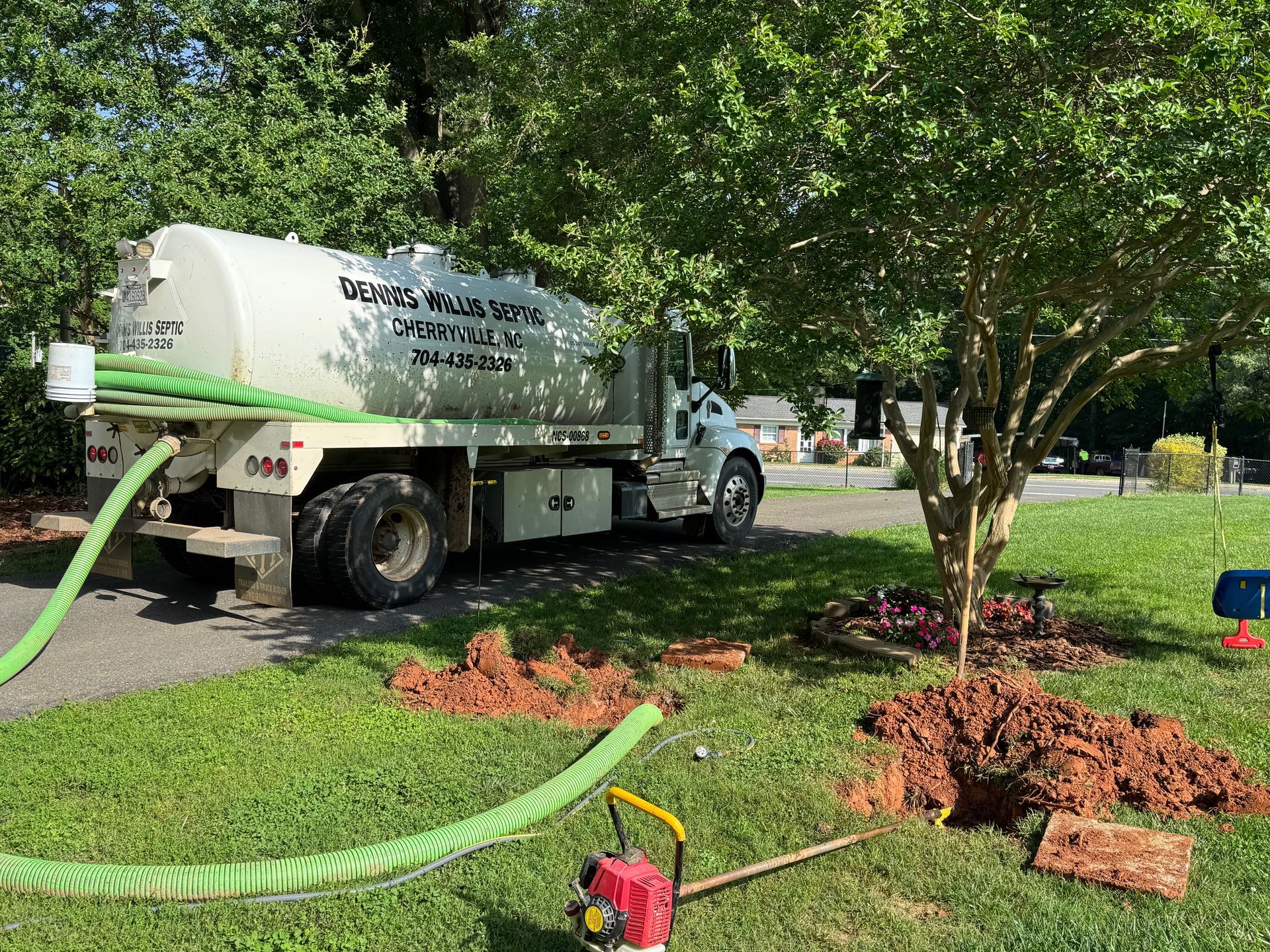 A person is pumping water into a septic tank with a green hose.