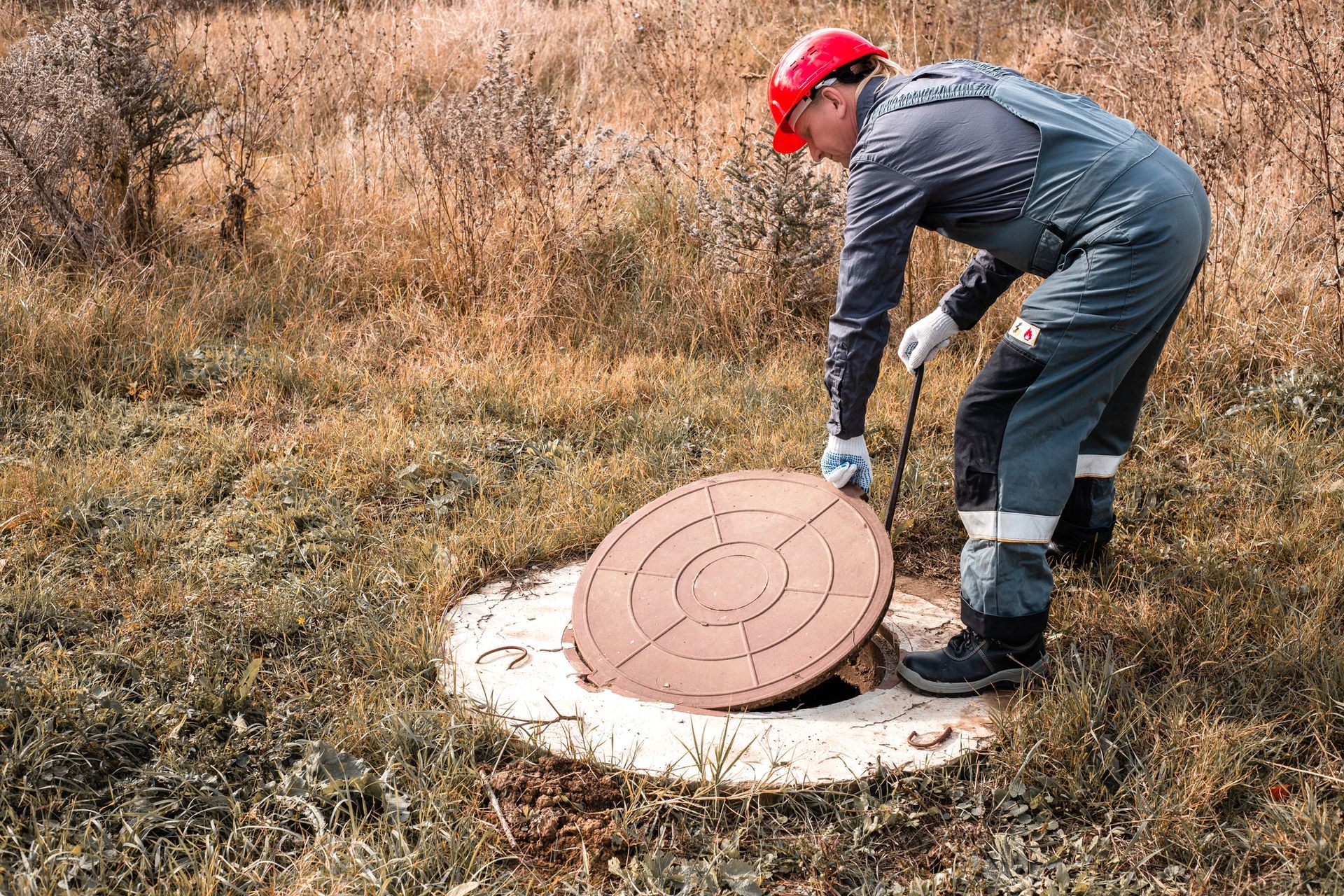 A man is opening a manhole cover in a field.