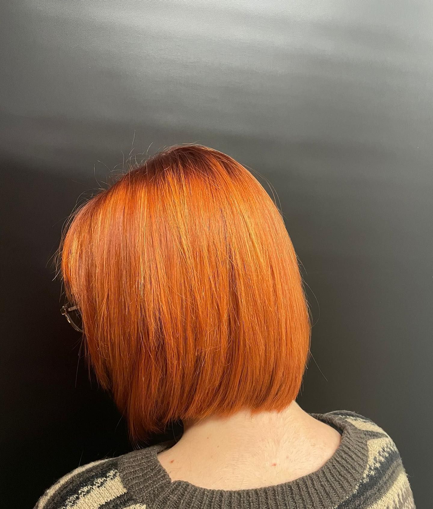 Schiena di donna con acconciatura a caschetto arancione brillante su sfondo scuro, che indossa un maglione fantasia.