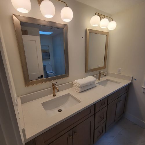 A bathroom with two sinks , two mirrors and a toilet.