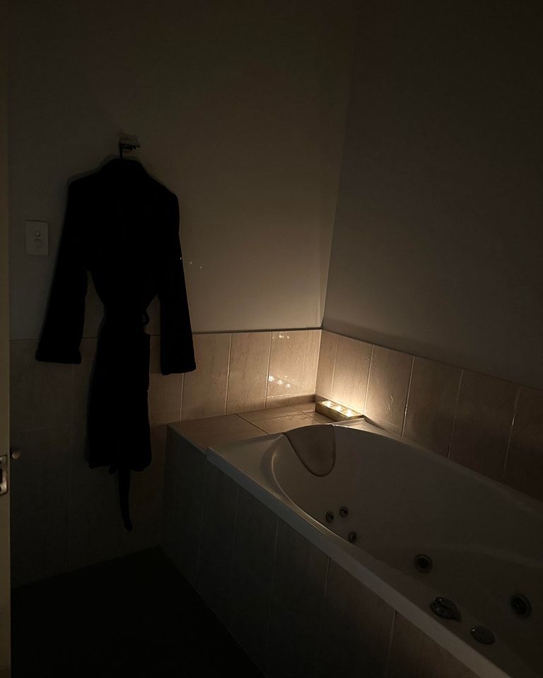 Dark bathroom scene with a robe hanging on the wall beside a lit bathtub.— Sage Spa & Beauty in Mackay, QLD