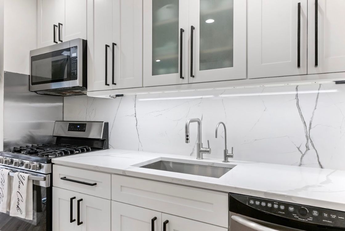 A kitchen with white cabinets , stainless steel appliances , a sink , stove and microwave.