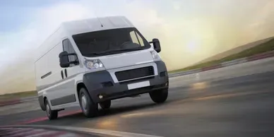 White delivery van driving on a race track, leaning into a curve with a sunny sky in the background.