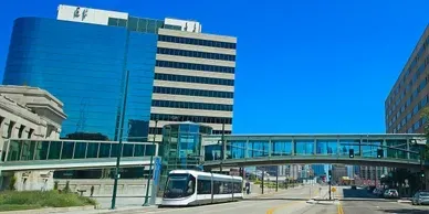 A city scene with a tram, skywalk, and blue glass buildings.