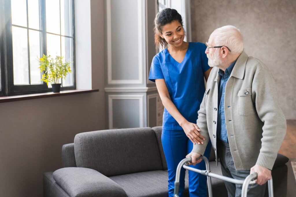 Portrait of a female young nurse helping an old male patient to walk using walker equipment in the bedroom.