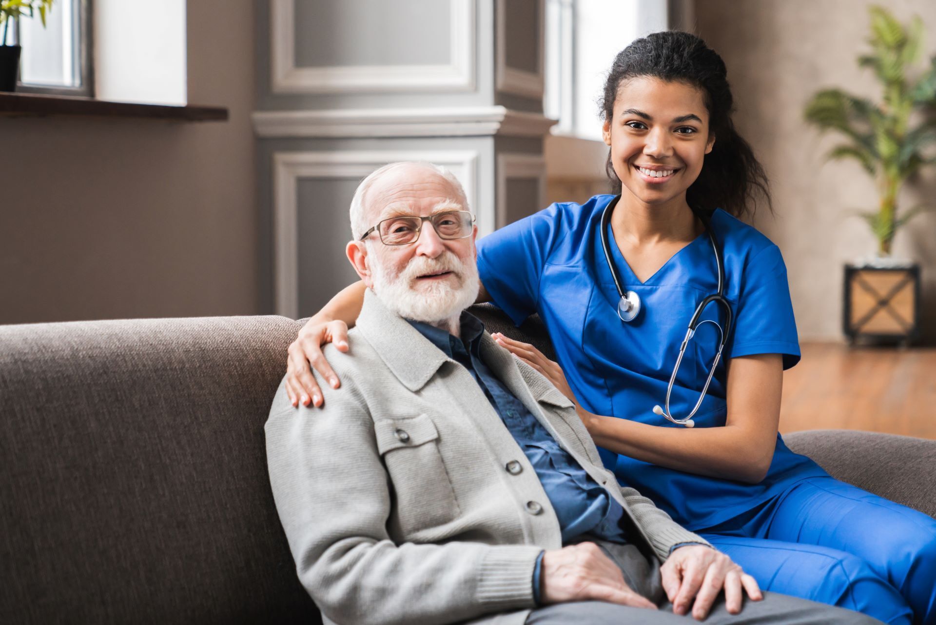 caregiver and patient sitting on couch looking at camera smiling