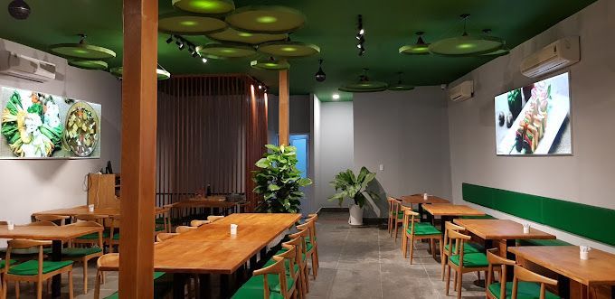 The modern interior of Sen Vegan House in Ho Chi Minh City, featuring wooden tables, green decor, and nature-inspired elements.