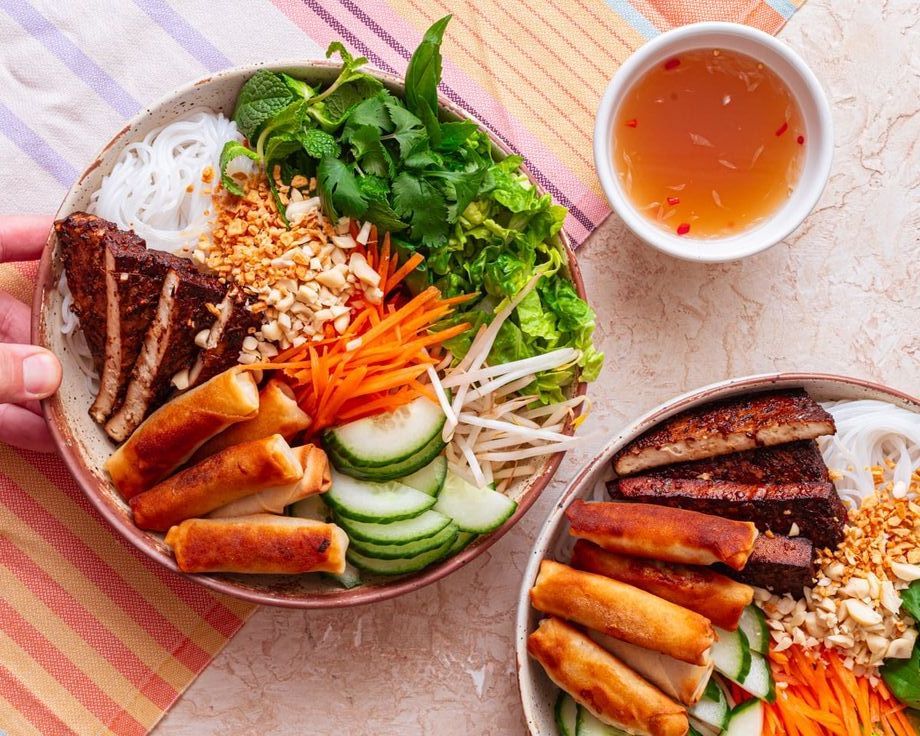 A colorful Vietnamese vegan noodle bowl (bún chay) with rice vermicelli, crispy spring rolls, grilled tofu, fresh herbs, and dipping sauce.