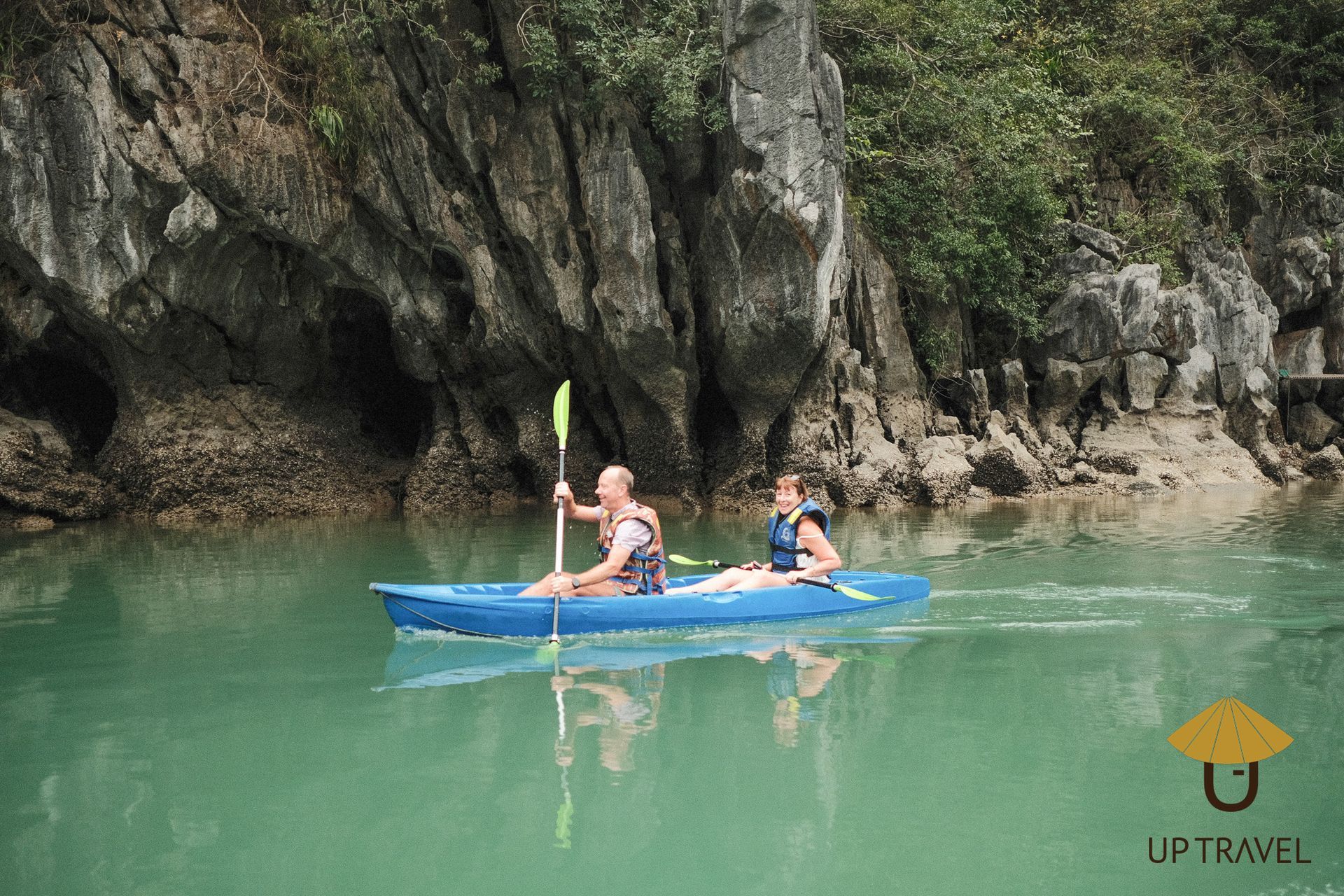 Couple kayaking on calm turquoise waters surrounded by towering limestone formations in Ha Long Bay, Vietnam.