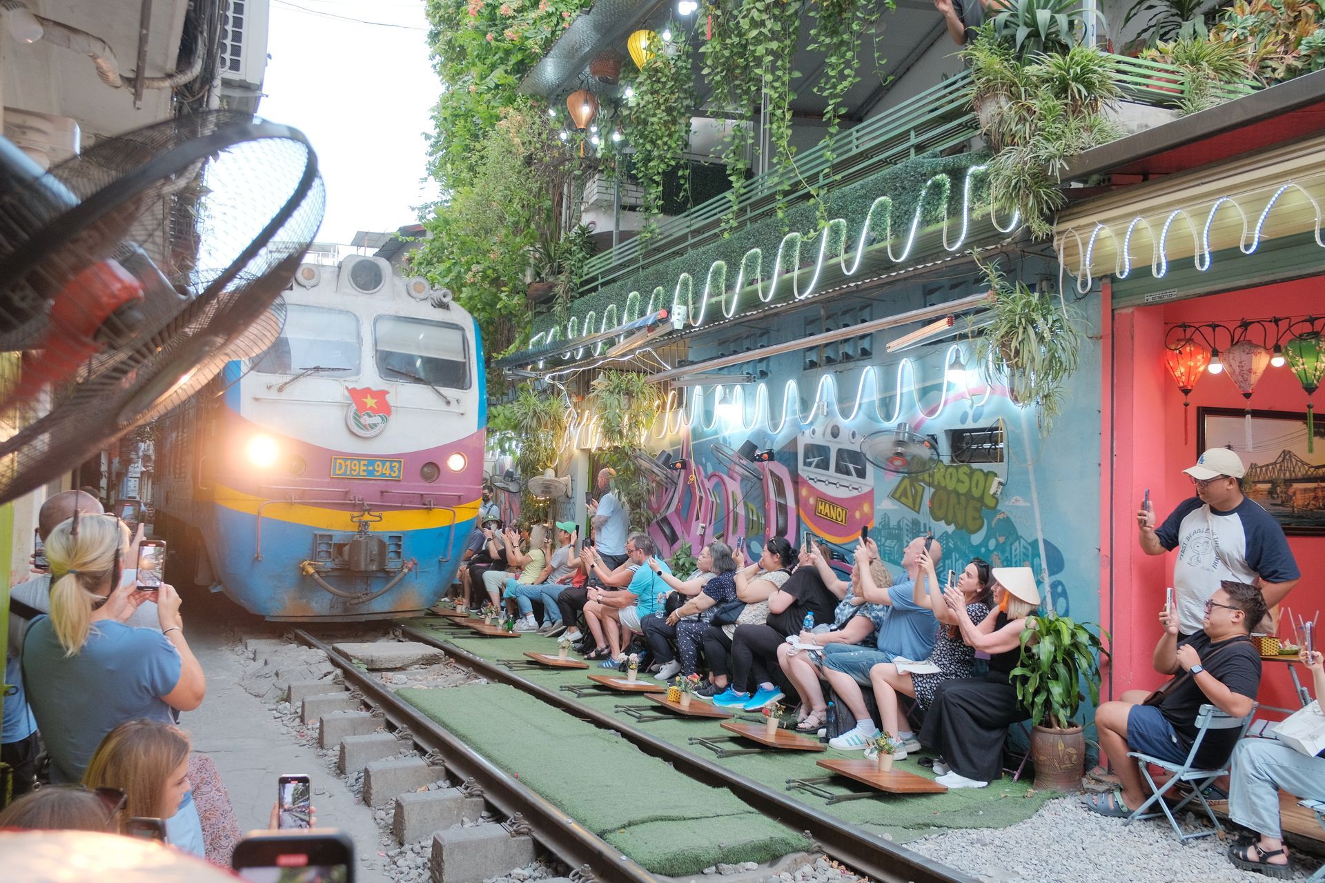 Travelers enjoying the unique experience of Hanoi’s famous Train Street, sitting at a cozy café as a train passes by.