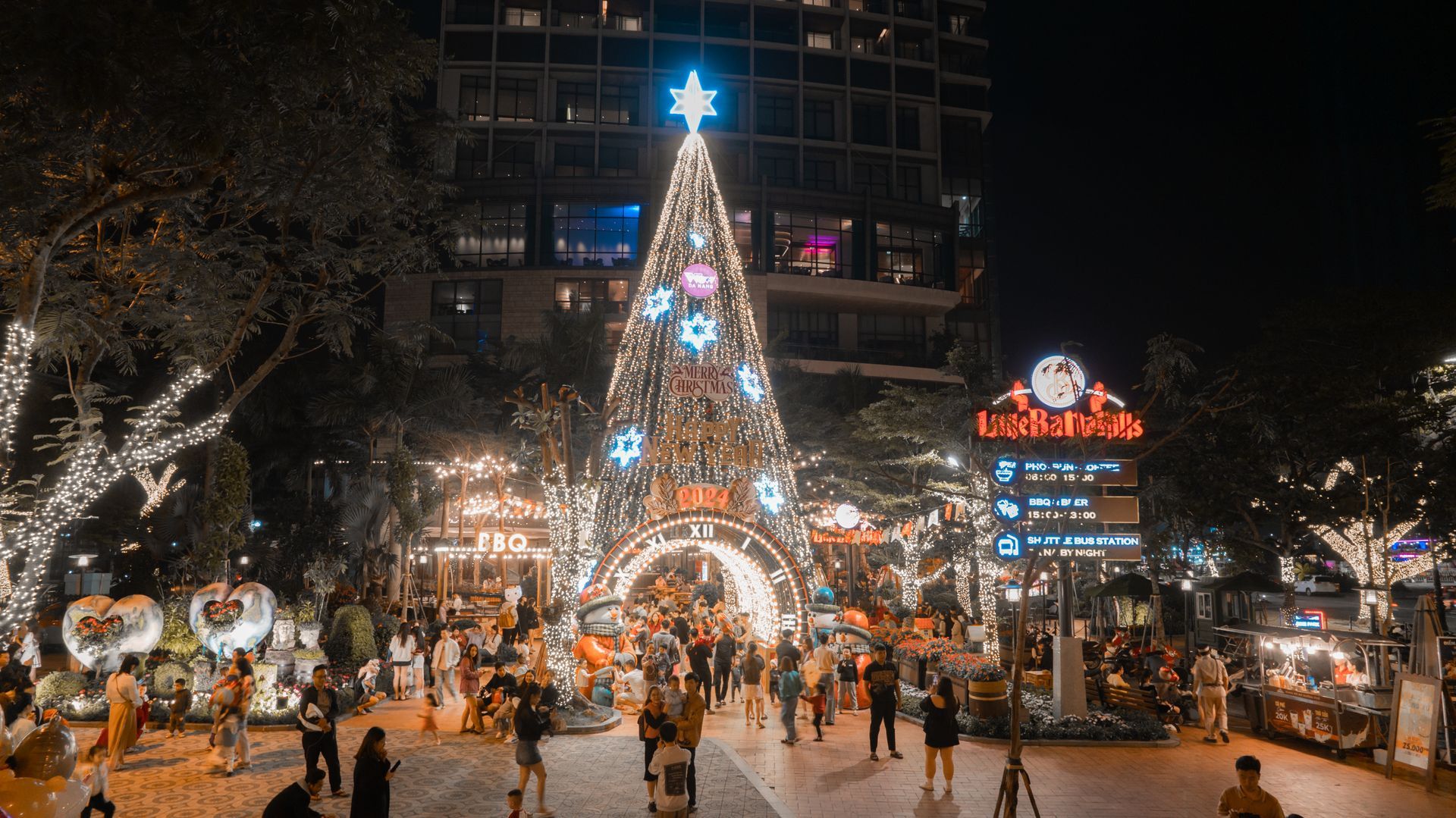 Night scene of Saigon’s holiday celebration with a giant Christmas tree, lights, and crowds enjoying the festive decorations.