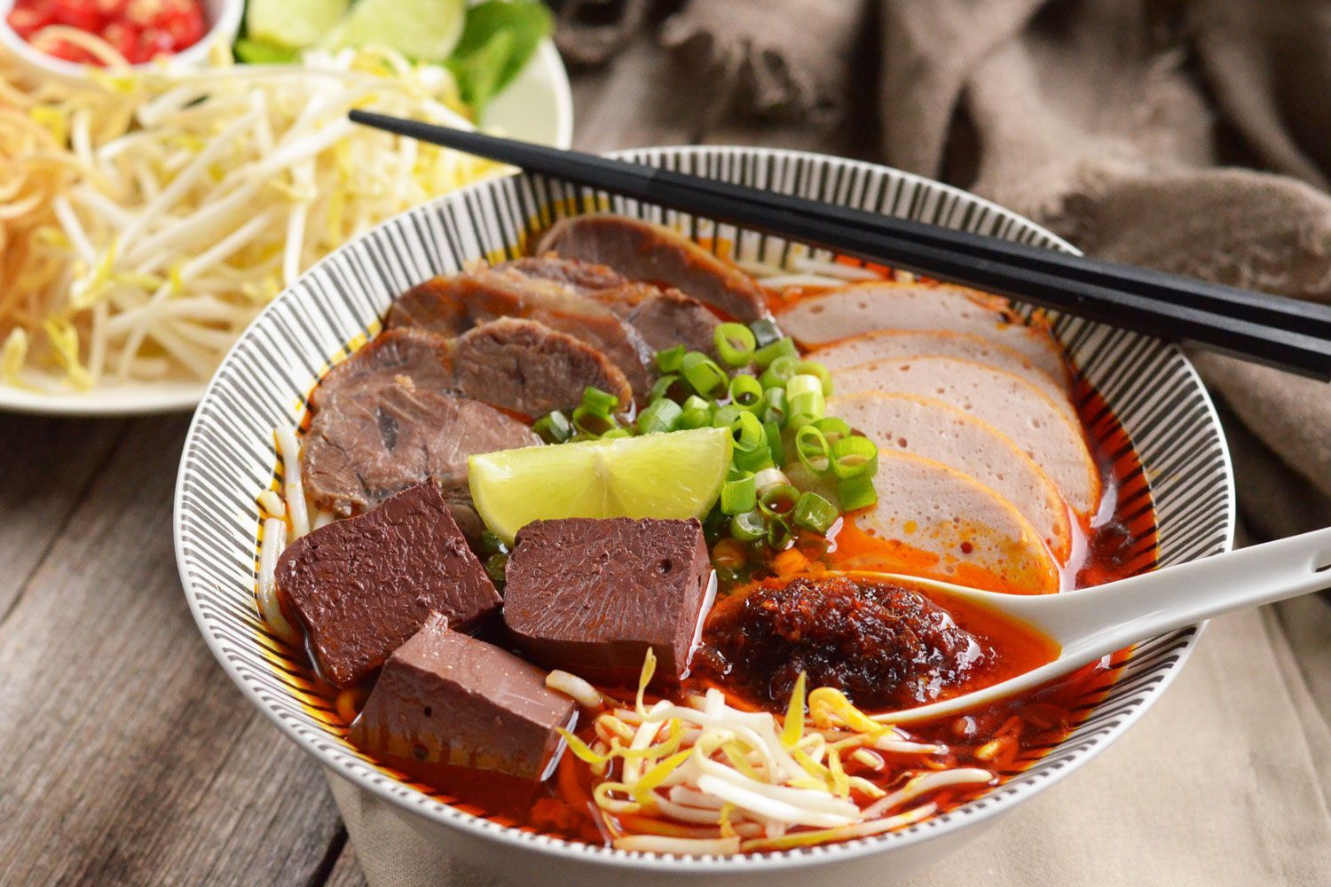 Vietnamese Hue beef noodle soup with pork roll, herbs, and chili oil.