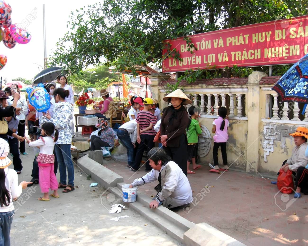 Street scene in Vietnam showing locals and a beggar near a temple entrance.