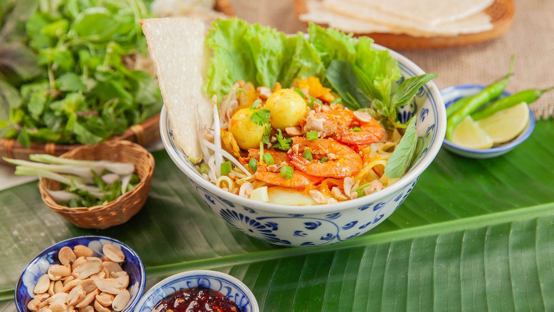 Bowl of Quảng noodles with shrimp, quail eggs, peanuts, and herbs.