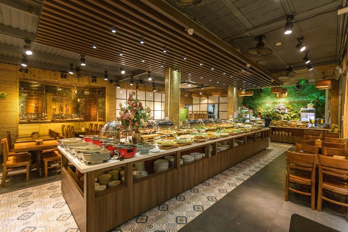 A spacious vegan buffet restaurant with warm wooden interiors, an elegant food display, and a lush green wall in the background.