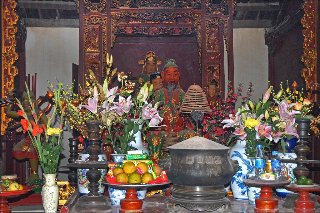 An ornate altar decorated with flowers, fruits, incense, and statues in a traditional Vietnamese temple.