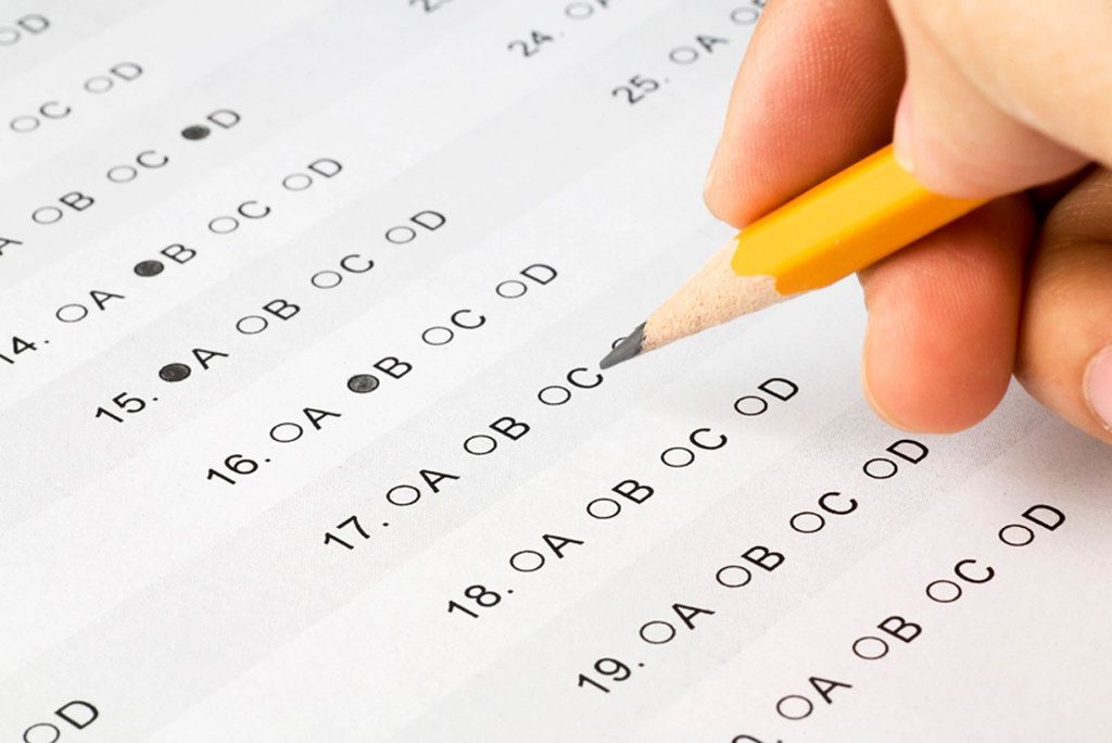 A close-up of a hand filling in circles on a multiple-choice exam sheet with a pencil.