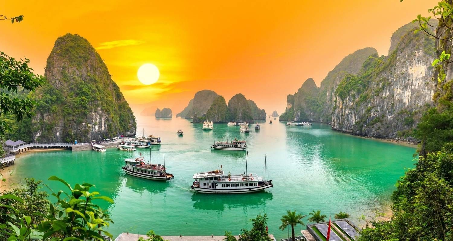 Afternoon sunlight over Ha Long Bay with cruise boats gliding through emerald waters and limestone cliffs.