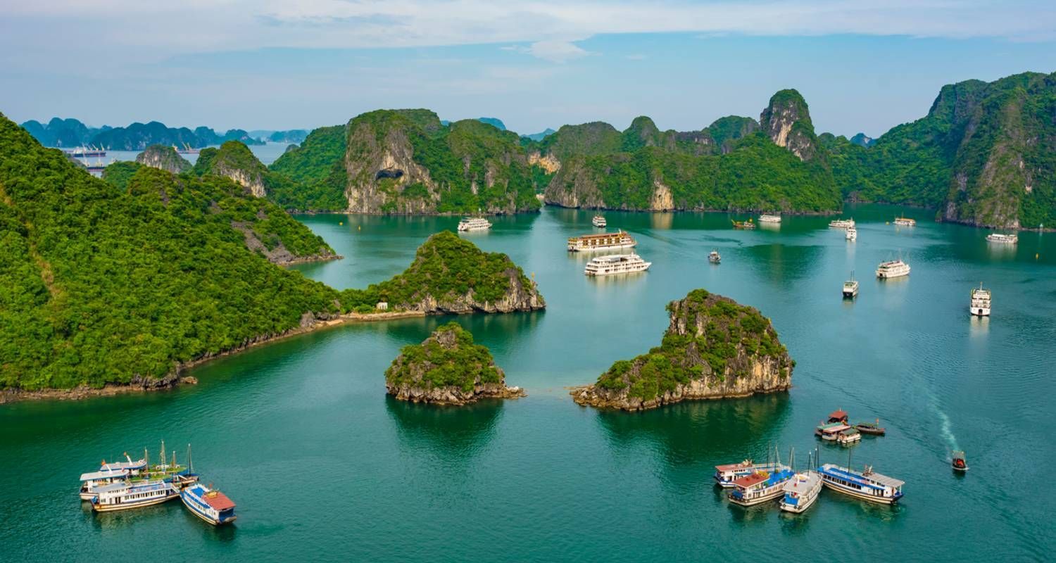 Aerial view of Ha Long Bay with limestone islands and white cruise boats sailing between them.