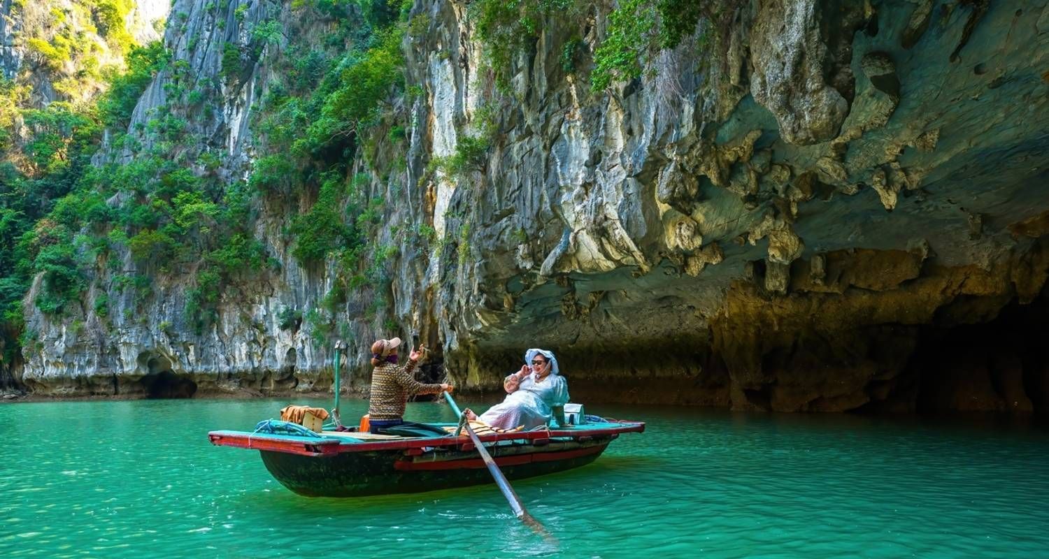 Tourists on a small wooden boat rowed by a local woman beneath towering cliffs in Ha Long Bay.