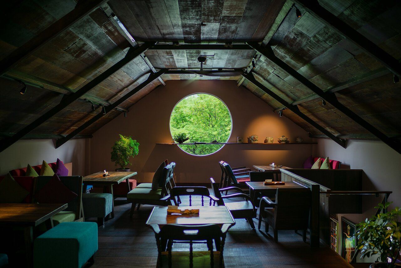 The cozy and elegant interior of Hum Signature in Ho Chi Minh City, featuring wooden furniture, warm lighting, and a circular window framing lush greenery.