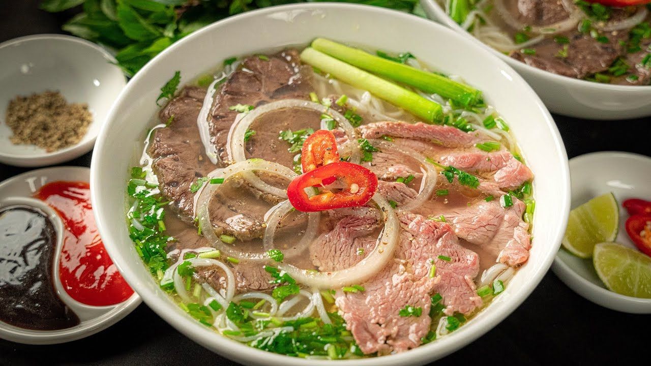 Bowl of Vietnamese beef phở with fresh herbs, chili, and lime.