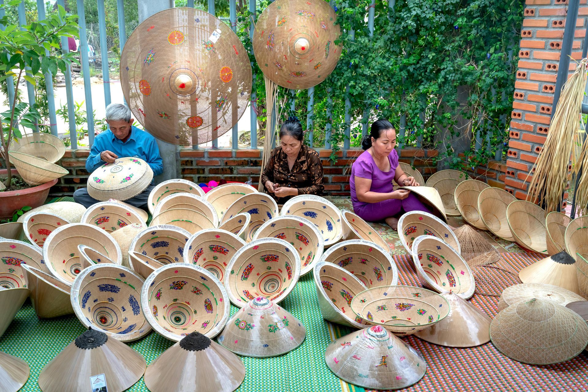 Artisans are carefully crafting traditional Vietnamese conical hats using palm leaves and bamboo frames.