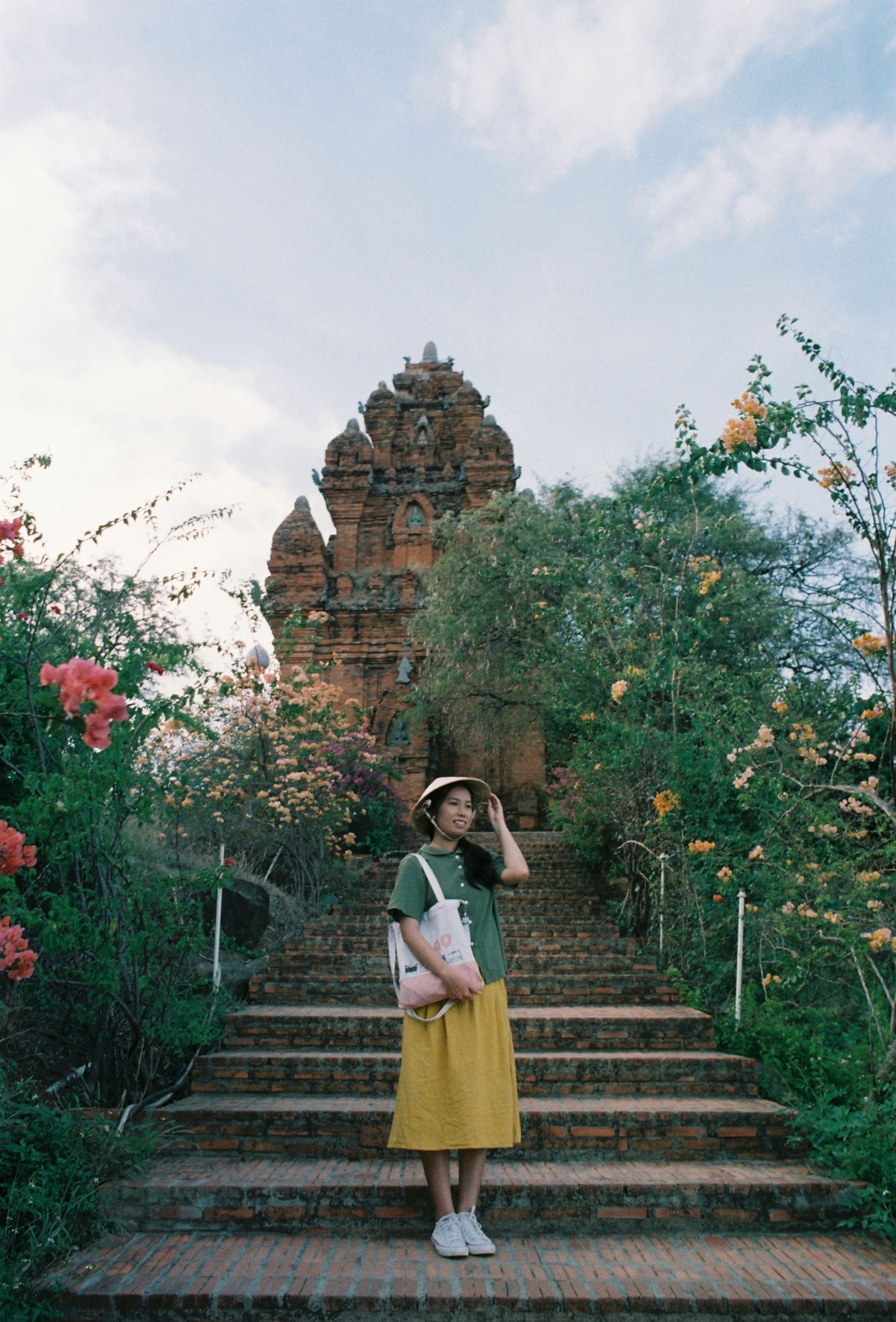 A visitor standing in front of the historic Po Nagar Cham Towers, surrounded by traditional architecture and greenery in Nha Trang, Vietnam.