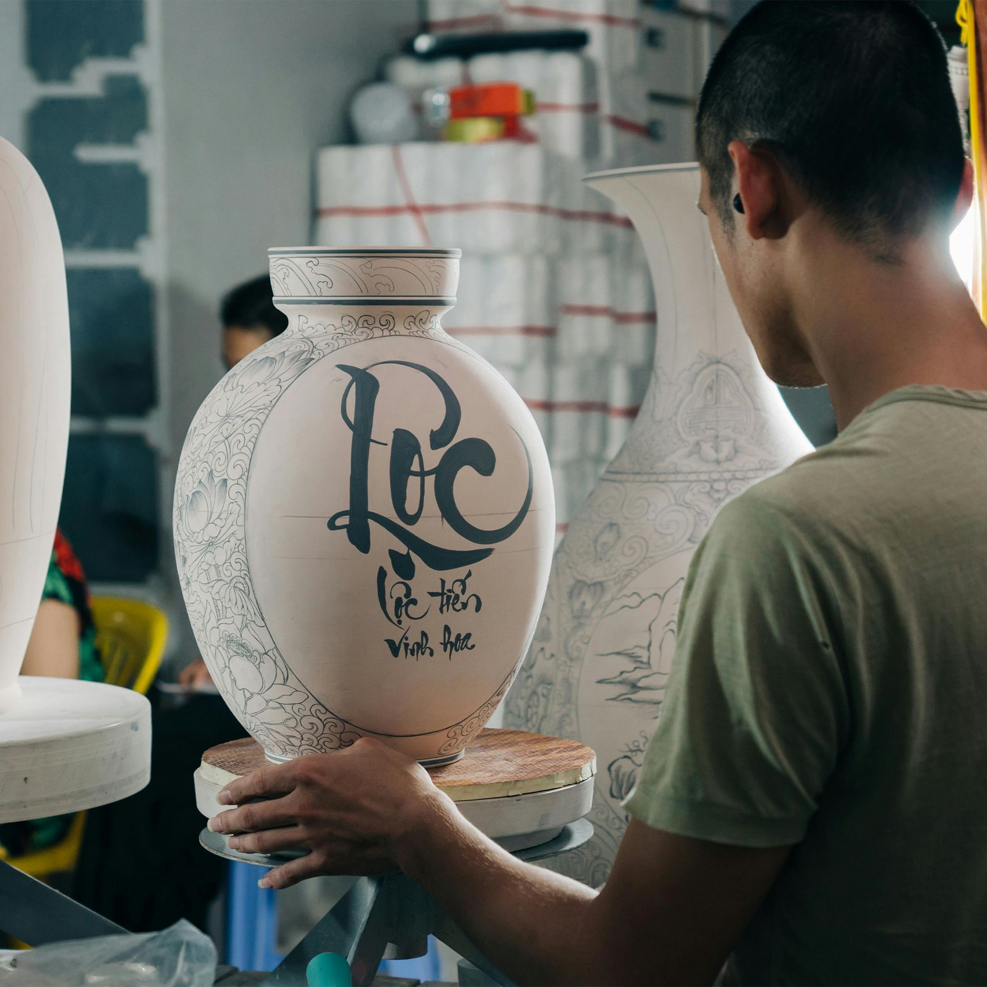 A ceramic artisan is meticulously decorating a handmade ceramic vase.