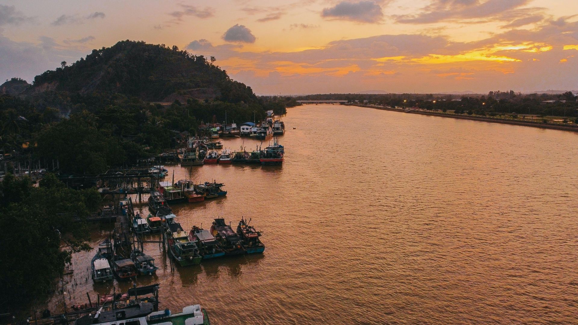 Fishing boats anchored along a river at sunset, surrounded by rolling hills in southern Vietnam.