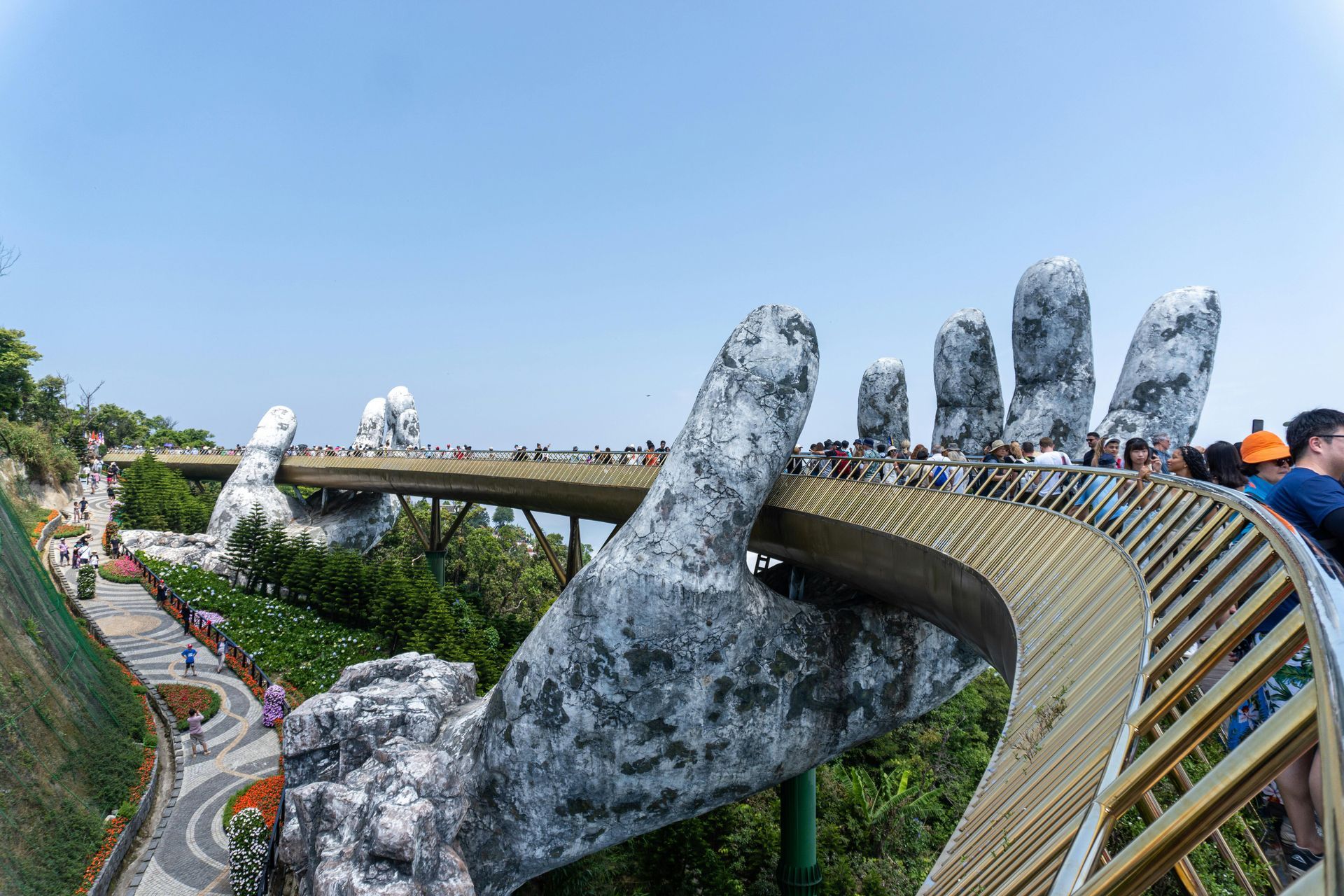 The Golden Bridge in Da Nang, Vietnam, held up by two giant stone hands amidst green mountains.