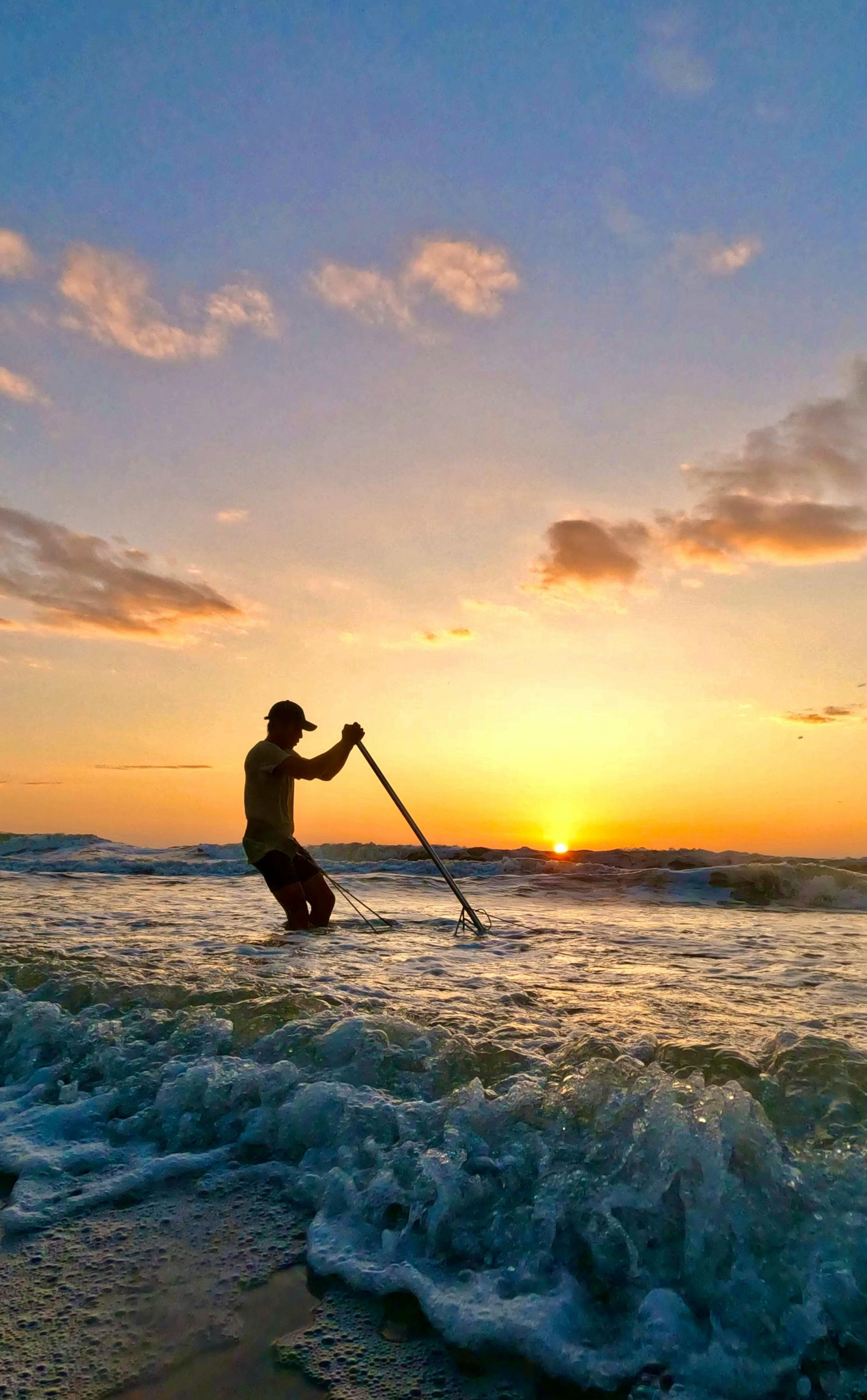 A man paddleboarding on the ocean at sunrise, silhouetted against the golden sky.
